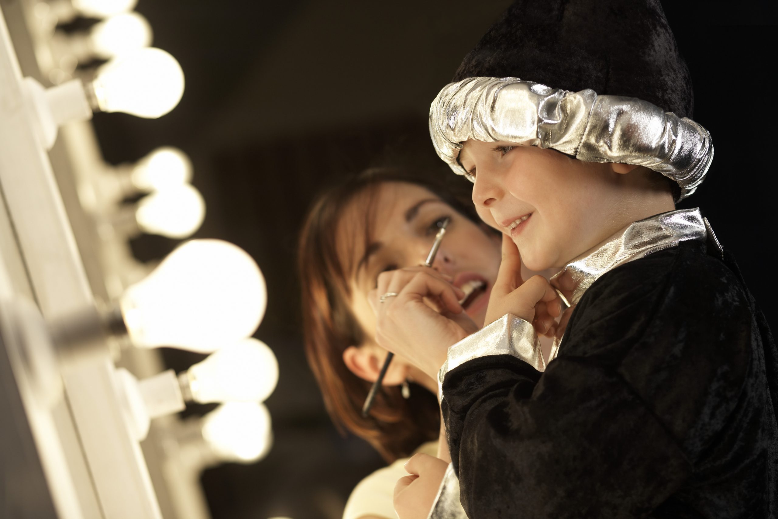 Teacher applying make-up to boy (3-5) in wizard costume backstage